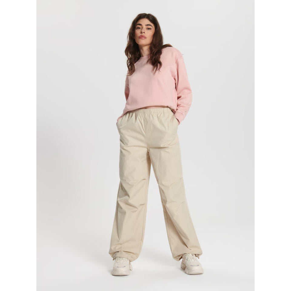 A woman modeling a light pink long-sleeve sweatshirt and beige wide-leg pants against a plain light gray studio background.