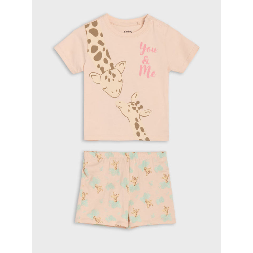A two-piece children's pajama set featuring a short-sleeve t-shirt and matching shorts. The t-shirt is a pale peach-pink with a large brown giraffe illustration and pink 'You & Me' text.