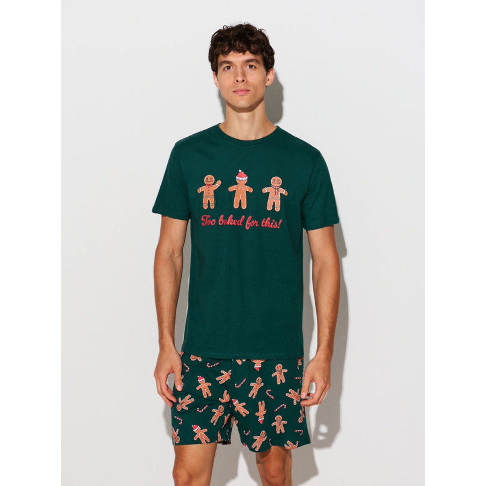 A man modeling a dark green short-sleeve t-shirt and matching shorts set. The t-shirt features three gingerbread men illustrations with the text 'So baked for that!' in red.