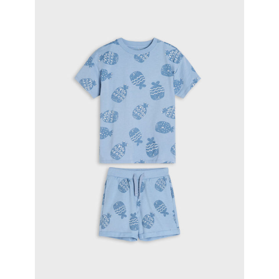 A two-piece kids' pajama set in light blue, featuring a short-sleeve t-shirt and matching shorts with an all-over pineapple print.