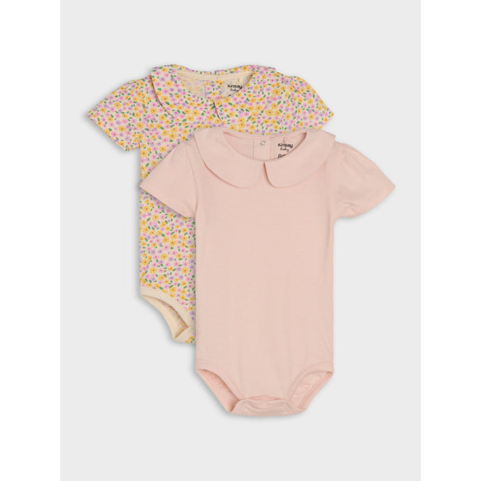 Two short-sleeve baby bodysuits stacked on a light gray background. The front bodysuit is light pink with a Peter Pan collar, and the back bodysuit has a small multicolor floral print on a pale pink base.