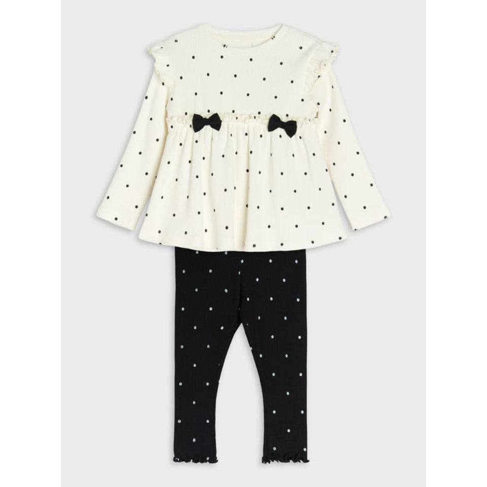 A toddler girl's two-piece outfit set featuring a cream long-sleeve peplum top with black polka dots and black bow accents, paired with matching black polka dot leggings.
