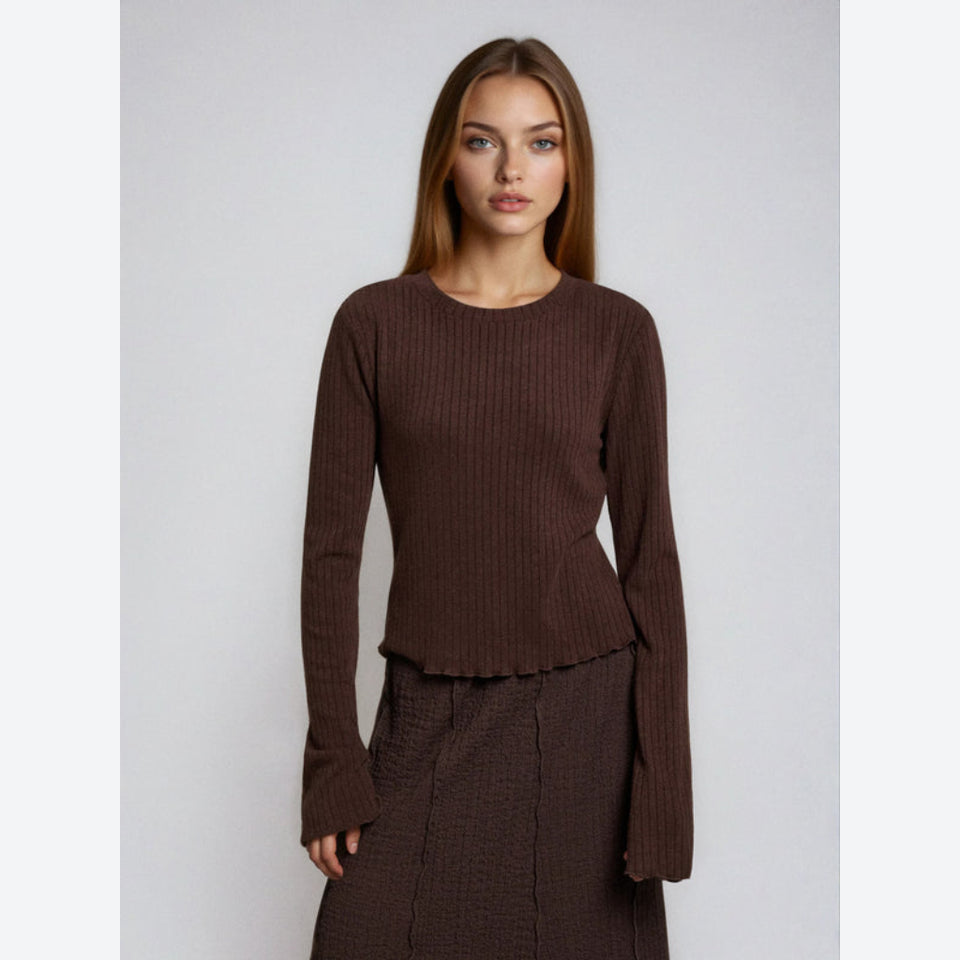 A woman modeling a dark brown ribbed knit long-sleeve top with a flared bell sleeves and a ruffled hem, paired with a matching brown textured skirt, against a plain light gray background.