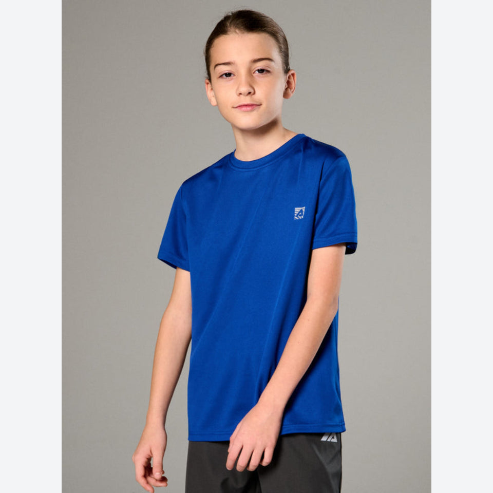 A boy modeling a royal blue short-sleeve athletic t-shirt with a small white logo on the left chest, paired with dark gray athletic shorts, against a solid gray studio background.