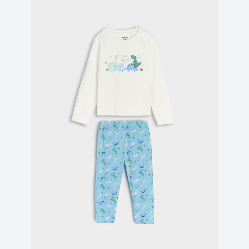 A children's two-piece pajama set featuring an off-white long-sleeve top with a green and blue dinosaur graphic on the chest, paired with light blue pants covered in a small dinosaur print.