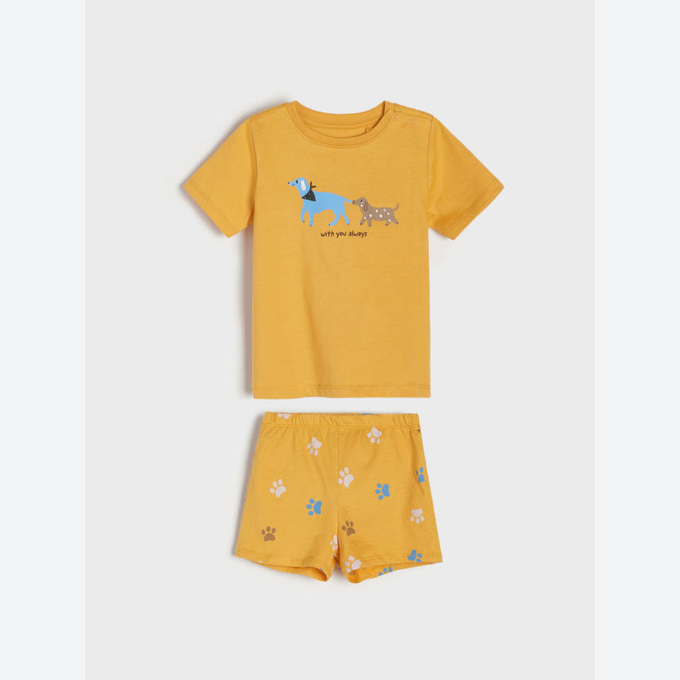 A toddler's two-piece pajama set consisting of a short-sleeve t-shirt and matching shorts in a warm mustard yellow color. The t-shirt features a graphic of two dogs with the text 'with you always' underneath.