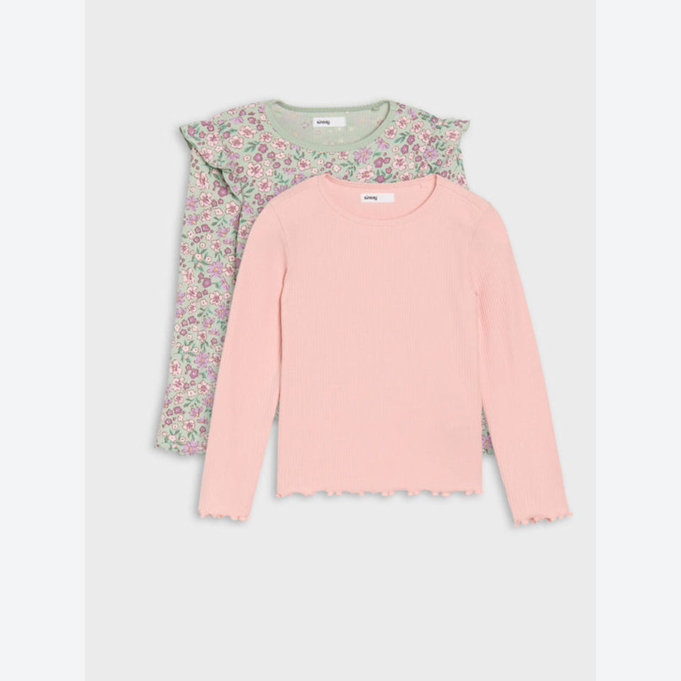 Two girls' long-sleeve tops laid flat on a light gray background. The front top is light pink with a scalloped hem, and the back top has a green base with a pink and white floral print and ruffled shoulders.