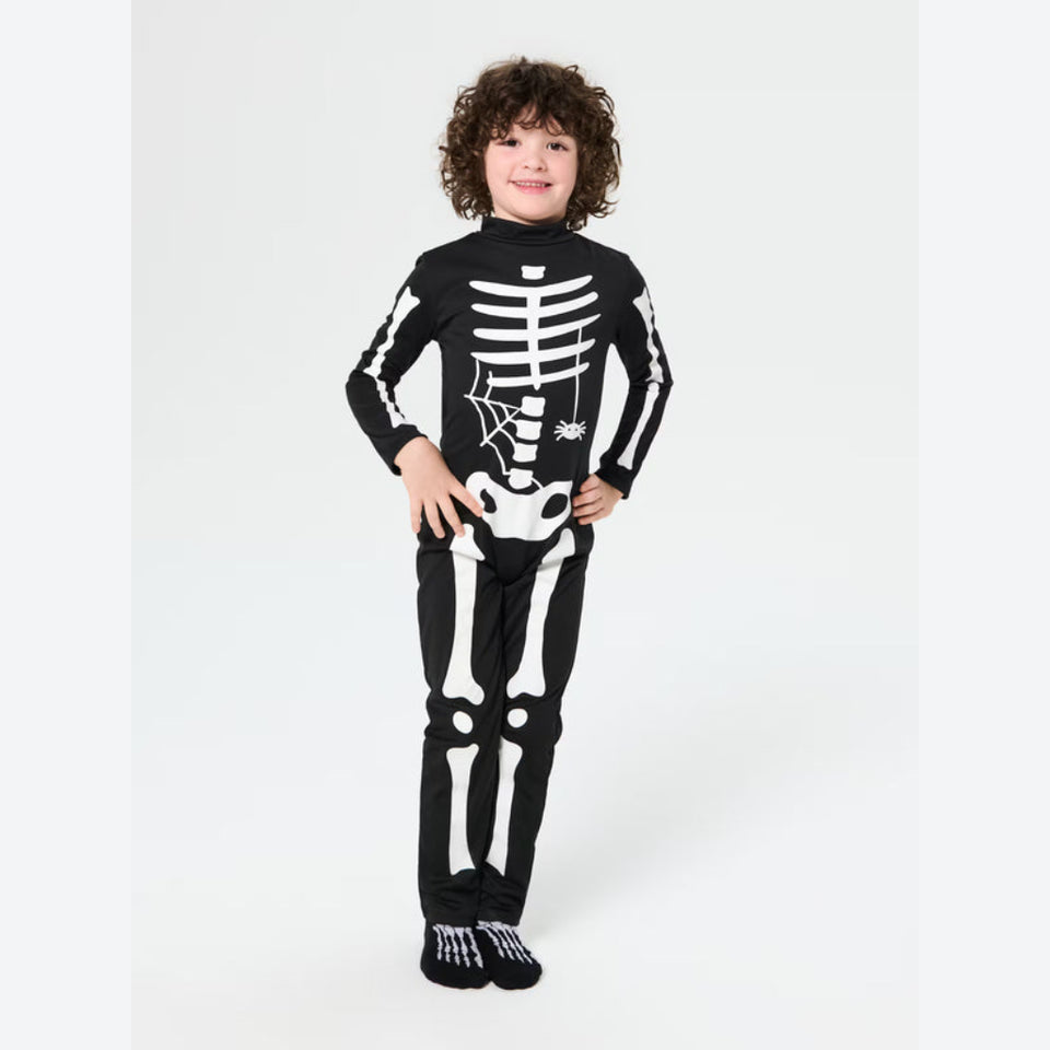 A child wearing a black and white skeleton-themed long-sleeve pajama set with matching socks, standing against a light gray studio background.