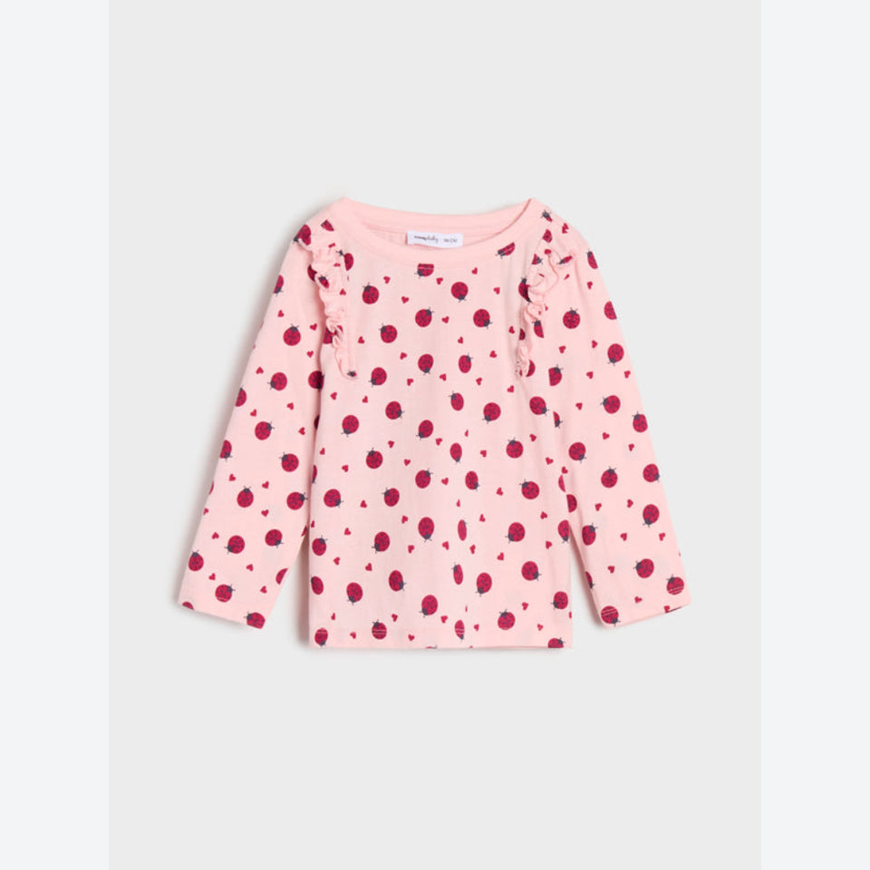 A pink long-sleeve baby top with an all-over raspberry print, featuring ruffle details on the shoulders and a small chest pocket, shown flat on a light gray background.