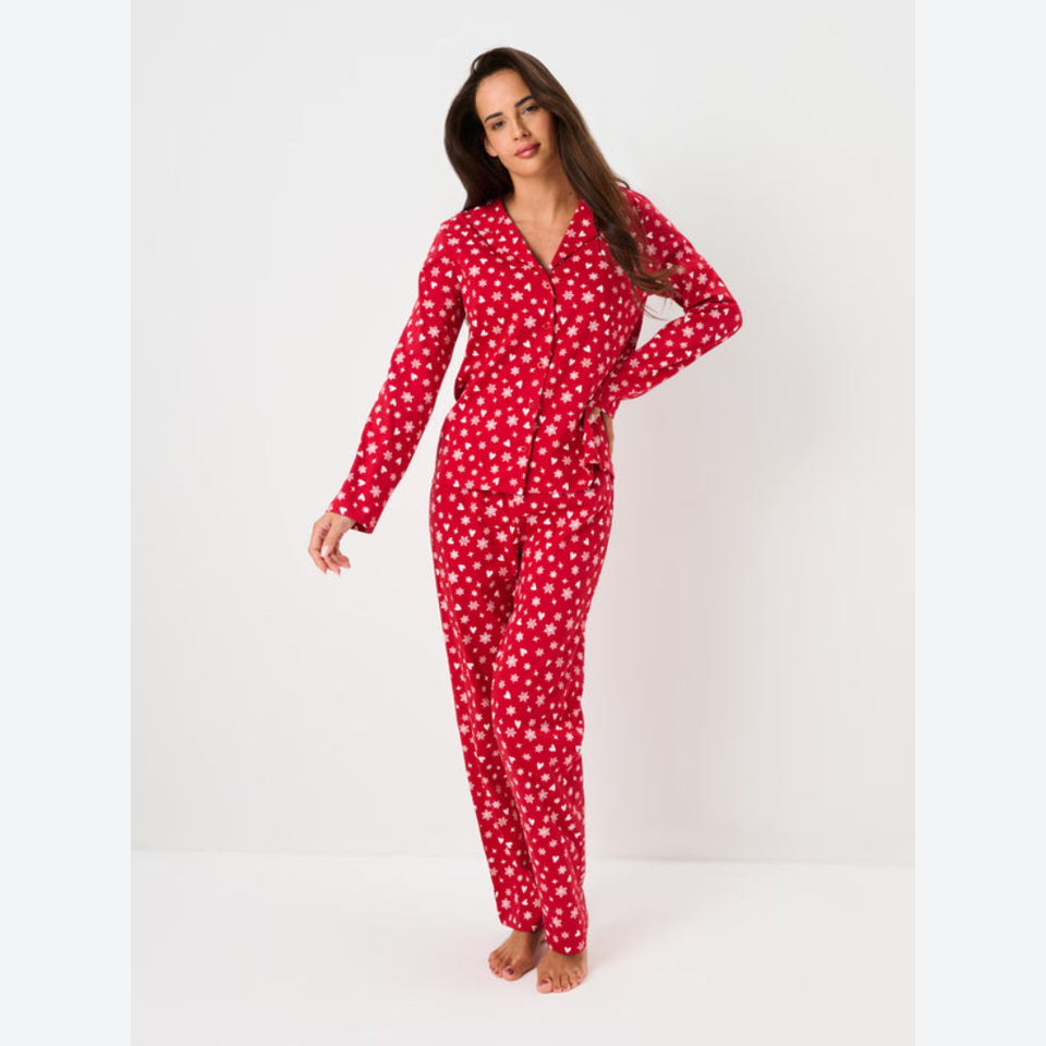 A woman modeling a red long-sleeve pajama set with a white dalmatian spot pattern, standing against a plain white studio background.
