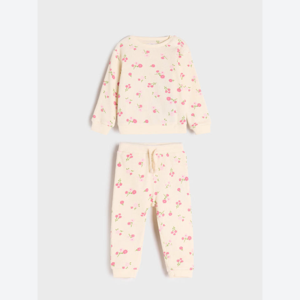A two-piece children's pajama set featuring a long-sleeve sweatshirt and matching jogger pants in a light cream color with a small pink and green floral print, laid flat on a light gray background.