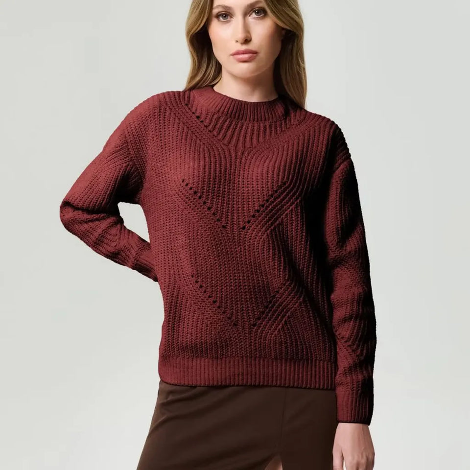 A woman wearing a textured, cable-knit crewneck sweater in a deep burgundy red, paired with a brown skirt, against a light gray studio background.