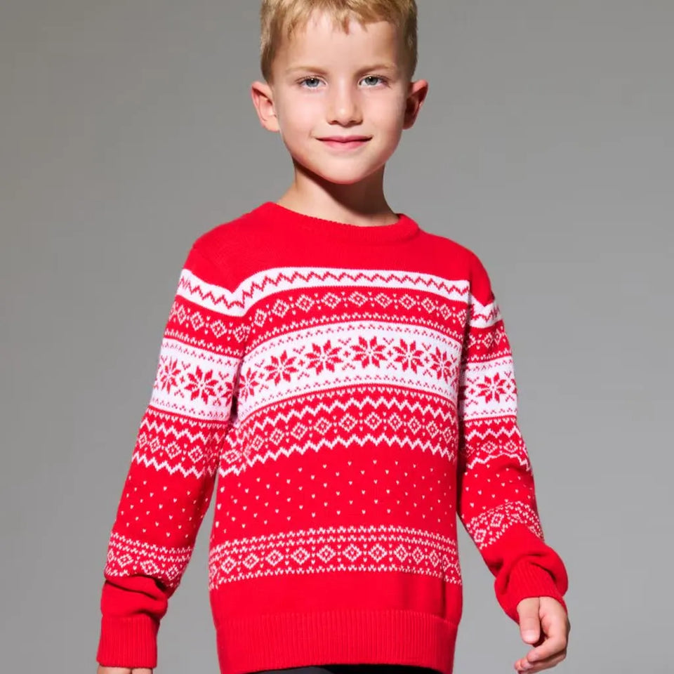 A young boy wearing a red and white patterned knit sweater, standing against a solid gray studio background.