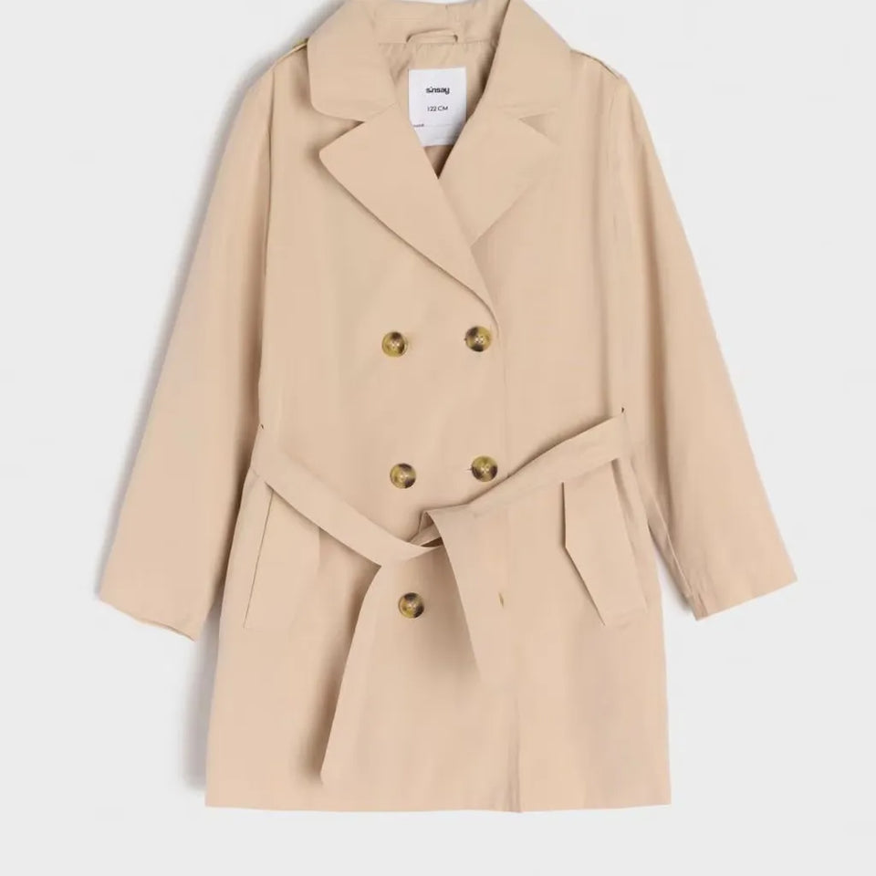 A beige double-breasted trench coat with a matching waist belt and brown buttons, shown against a plain light gray background.