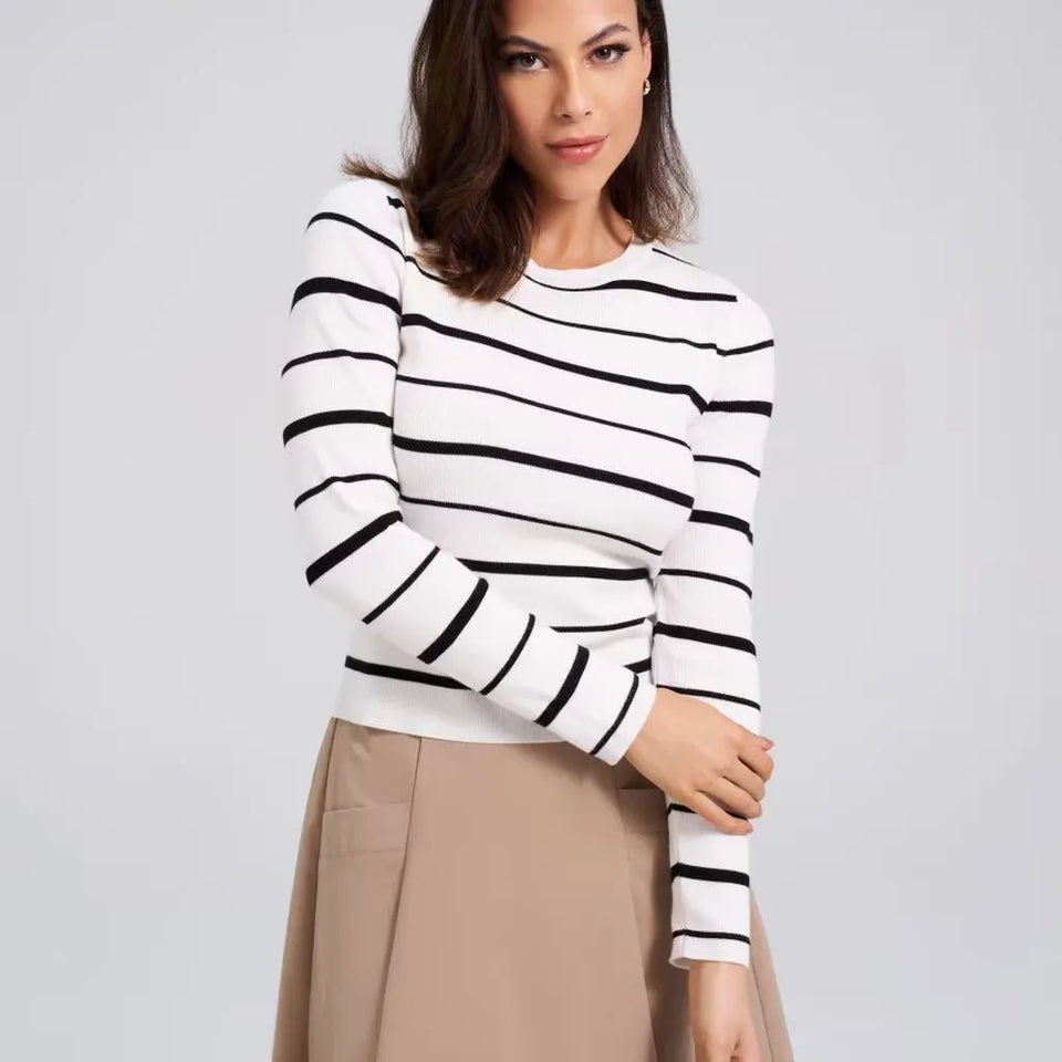 A woman wearing a fitted long-sleeve knit top with horizontal black stripes on a white background, paired with a beige skirt, against a light gray studio backdrop.