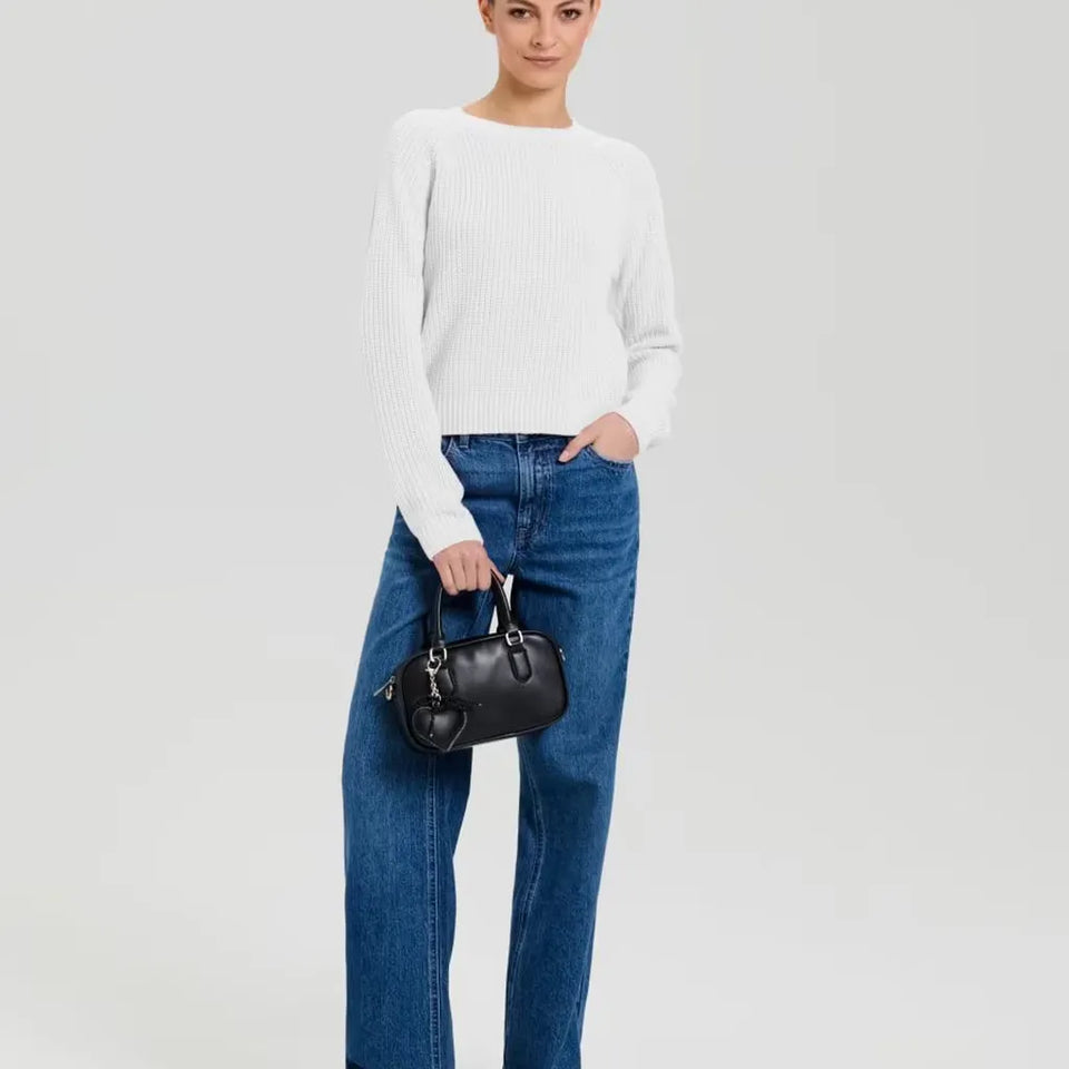 A model wearing a white ribbed knit long-sleeve top, blue jeans, and holding a small black leather handbag against a light gray studio background.