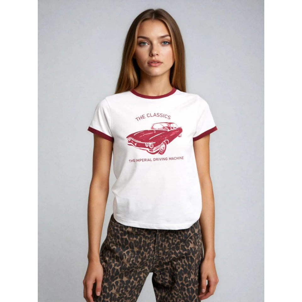 A woman modeling a white ringer t-shirt with red trim and a red graphic of a classic car and the text 'THE CLASSICS THE IMPERIAL DRIVING MACHINE' against a light gray studio background.