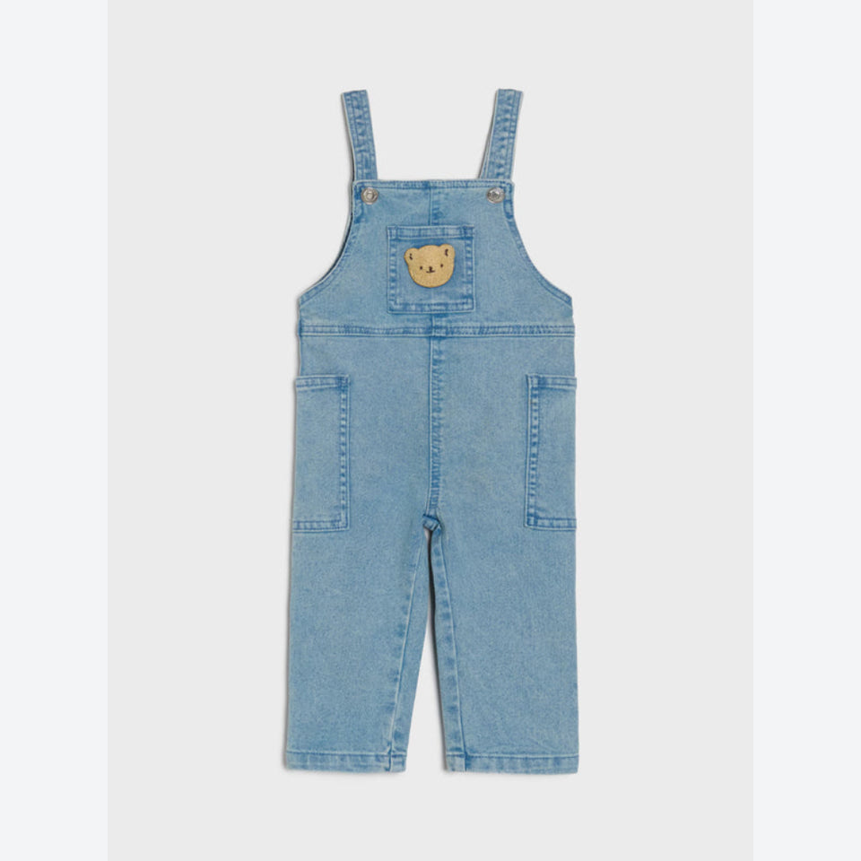 A pair of light blue denim baby overalls with adjustable shoulder straps, front patch pockets, and a small embroidered yellow bear face patch on the chest, shown flat against a light gray background.