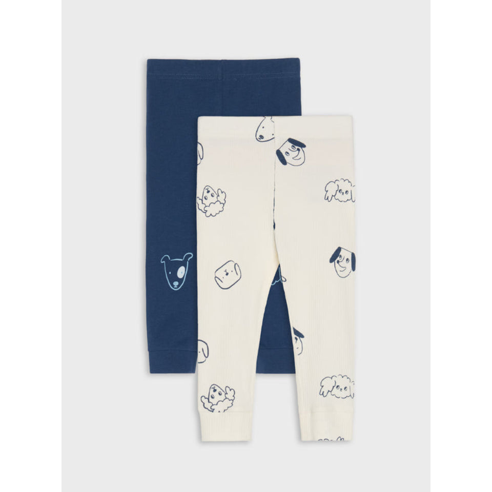 Two pairs of children's leggings laid flat on a light gray background. The front pair is cream with a navy blue cartoon dog and cloud print, and the back pair is solid navy blue.