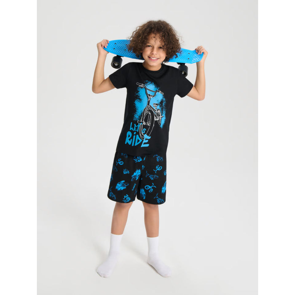 A child model wearing a black t-shirt and matching shorts with blue bicycle graphics, holding a blue skateboard over their shoulders against a light gray studio background.