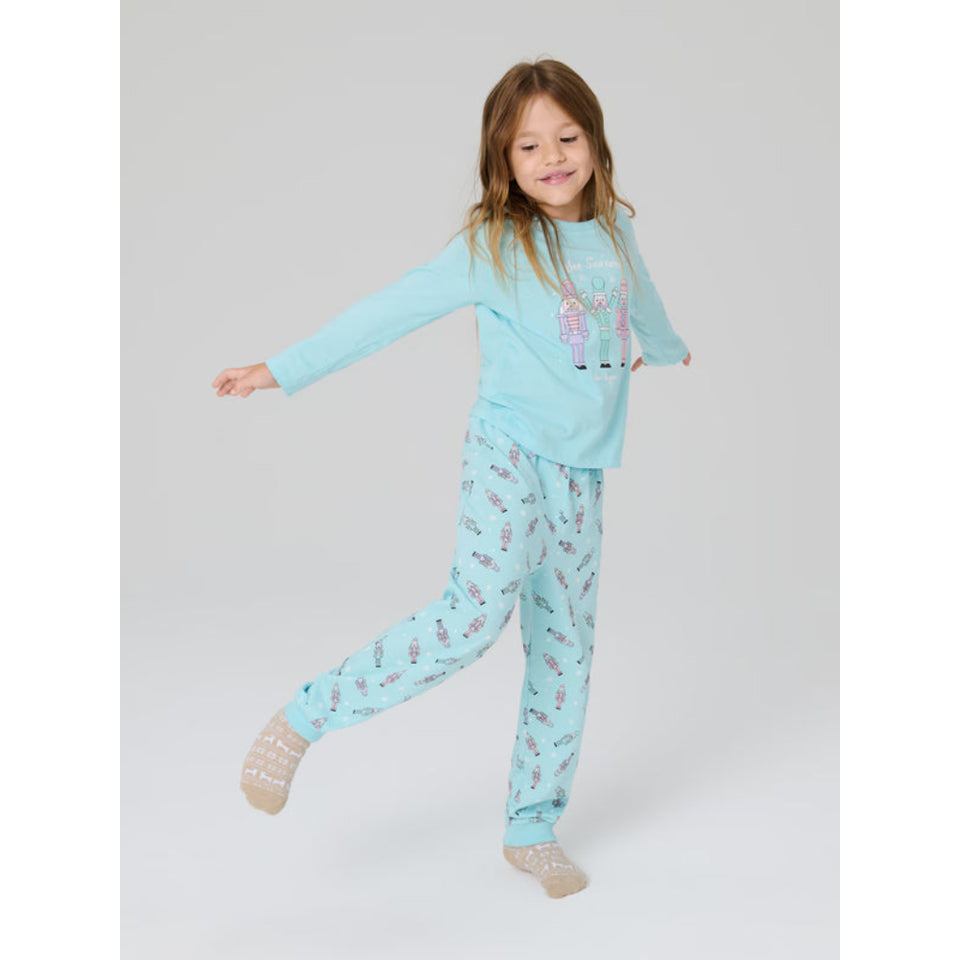 A young girl wearing a light blue pajama set with a bunny graphic on the top and a pastel patterned pair of pants, posing on a light gray studio background.