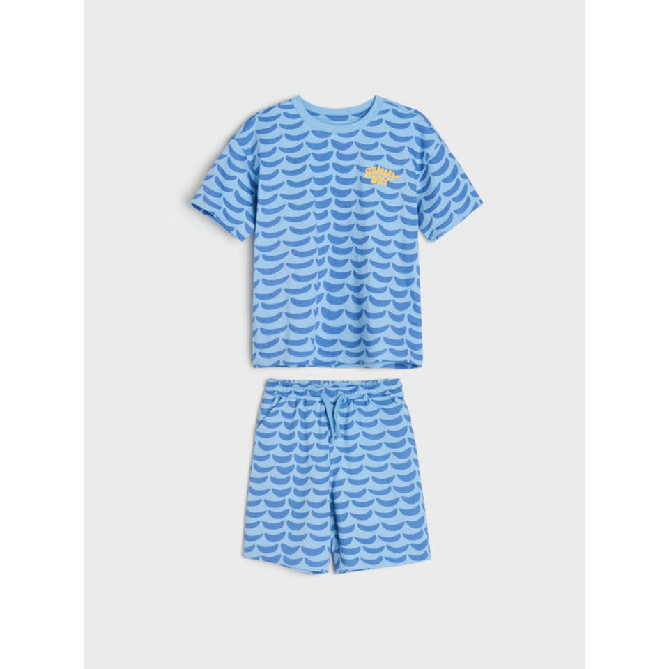 A two-piece kids' pajama set featuring a short-sleeve t-shirt and matching shorts in light blue with a darker blue scallop pattern and a small yellow crown graphic on the chest, displayed on a light gray background.