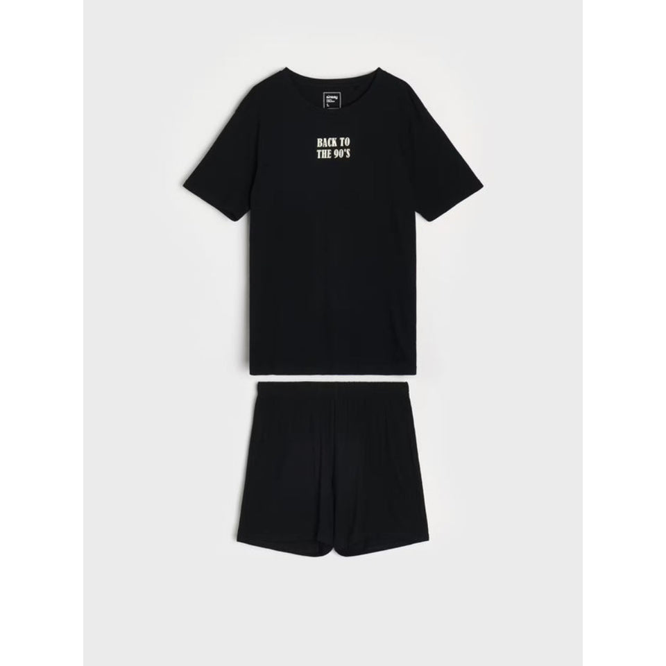 A two-piece black lounge set consisting of a short-sleeve t-shirt and matching shorts, laid flat on a light gray background. The t-shirt features the text 'BACK TO THE 90S' printed in white on the left chest.