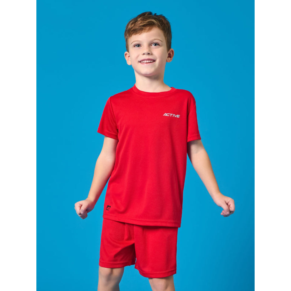 A young boy smiling and posing in a red athletic t-shirt and matching red shorts against a solid blue background. The t-shirt features a small white 'ACTIVE' logo on the left chest.