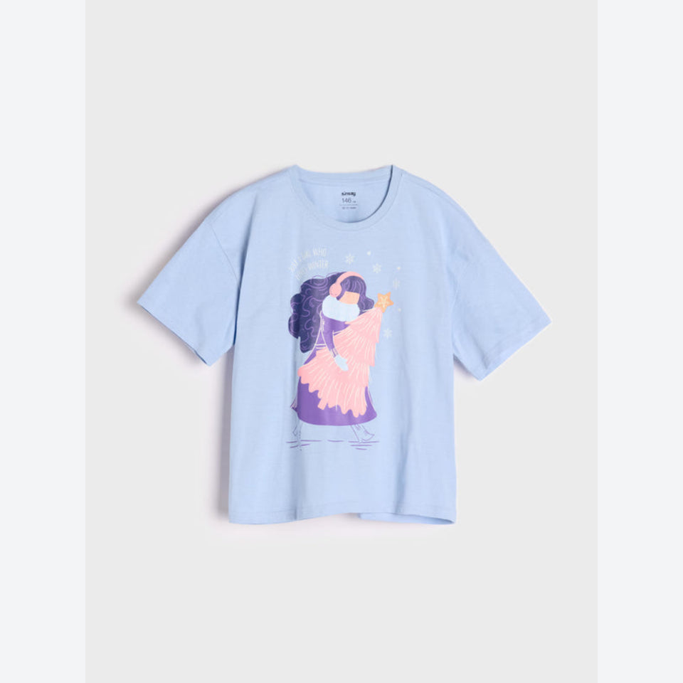 A light blue short-sleeve crewneck t-shirt featuring a colorful graphic print of a girl in a pink dress and purple headband, displayed against a light gray background.
