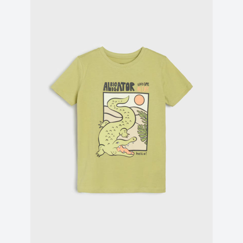 A light olive green short-sleeve t-shirt with a cartoon alligator graphic and the text 'ALIGATOR' and 'WILD LIFE' on the front, displayed flat against a light gray background.