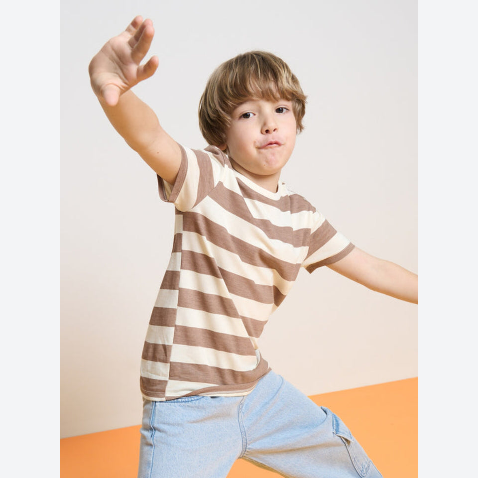 A young boy wearing a brown and cream striped short-sleeve t-shirt and light blue jeans, posing dynamically with one arm extended forward against a neutral studio background.