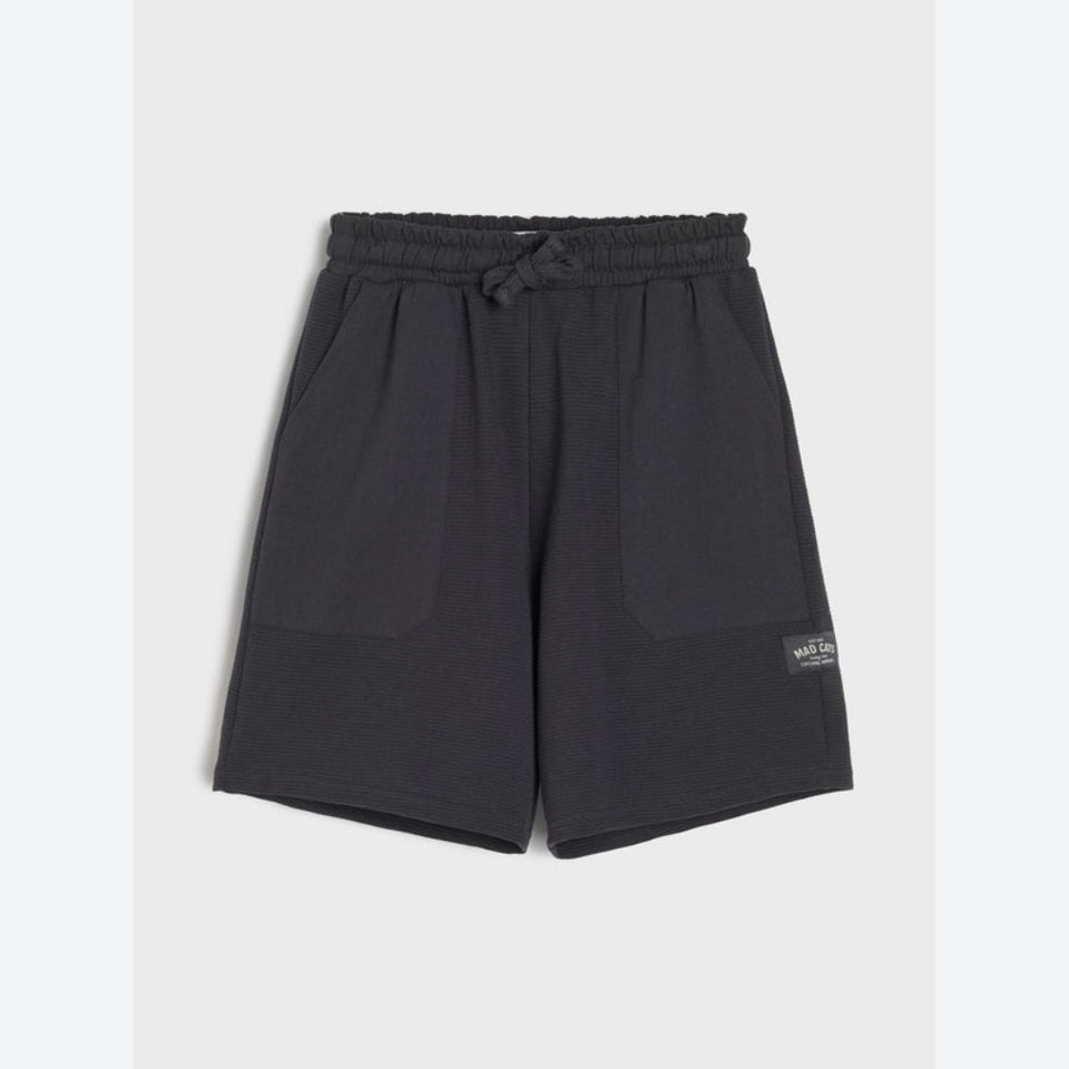 Black fleece drawstring shorts with side pockets and a small woven brand label on the lower left leg, shown flat against a light gray background.
