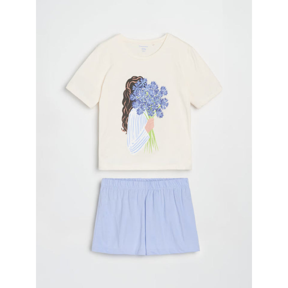A two-piece children's outfit set featuring a cream-colored short-sleeve t-shirt with a graphic of a girl holding blue flowers, paired with light blue shorts, displayed flat against a light gray background.