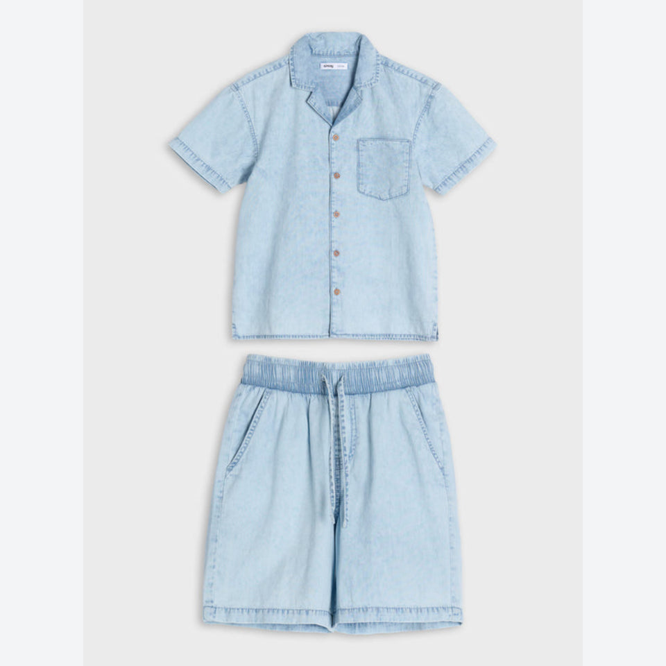 A light blue denim two-piece set for a child, featuring a short-sleeve button-up shirt with a chest pocket and matching drawstring shorts, laid flat against a light gray background.