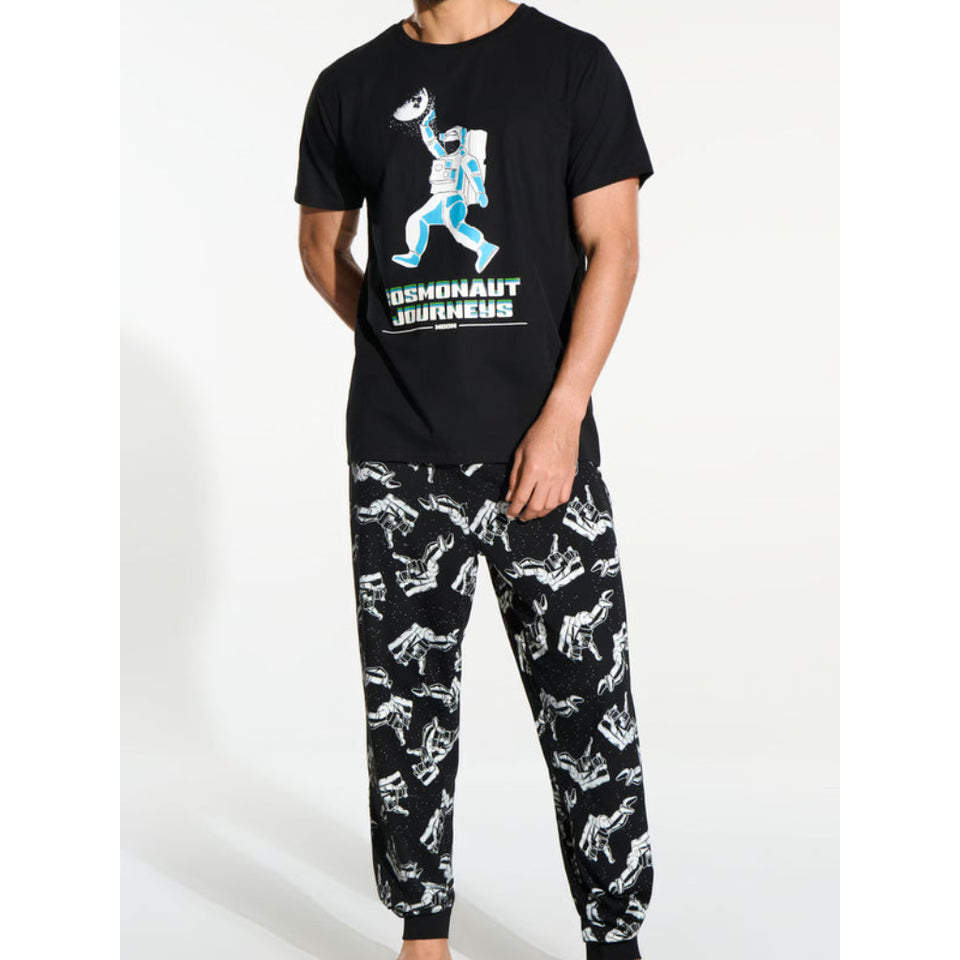 A man modeling a black short-sleeve t-shirt and matching black jogger pants with white dinosaur patterns. The t-shirt features a graphic of an astronaut carrying a moon and the text 'DEMONAUT JOURNEYS'.