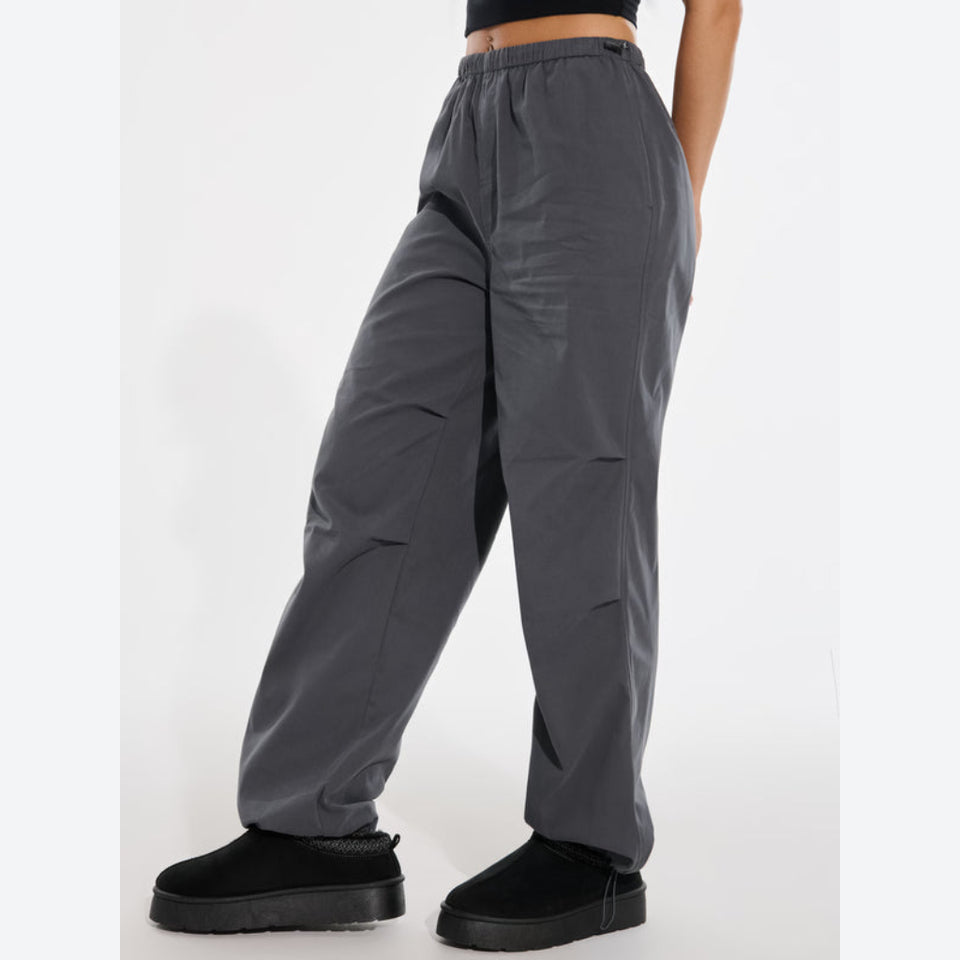 A person wearing loose dark gray wide-leg pants with an elastic waistband, paired with black slip-on shoes, shown from the waist down against a plain light background.