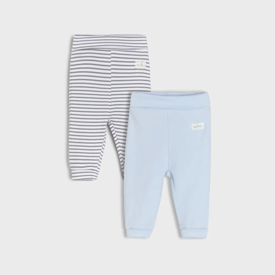 Two pairs of baby leggings laid flat on a light gray background: one pair is white with thin gray horizontal stripes, and the other is a solid pale blue. Each pair has a small white brand patch on the upper leg.