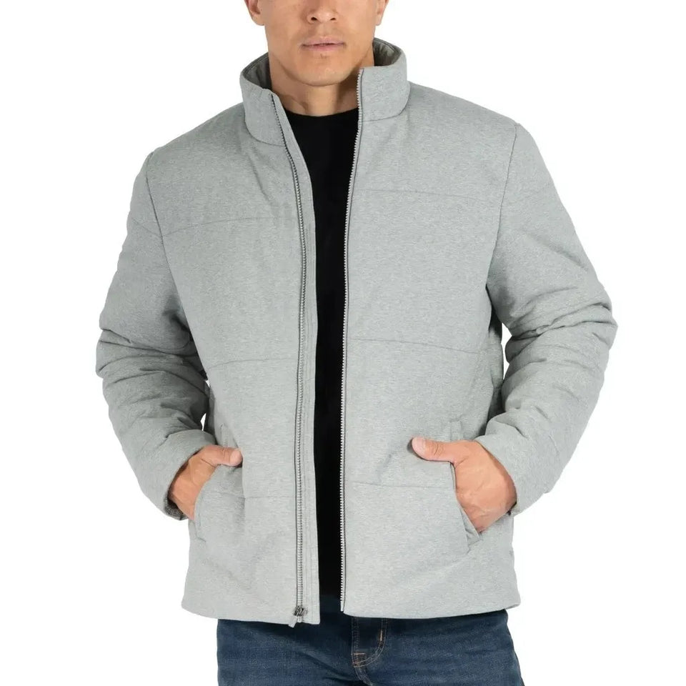 A man wearing a light gray zip-up jacket with a stand-up collar and front pockets, layered over a black shirt and blue jeans, against a plain white background.