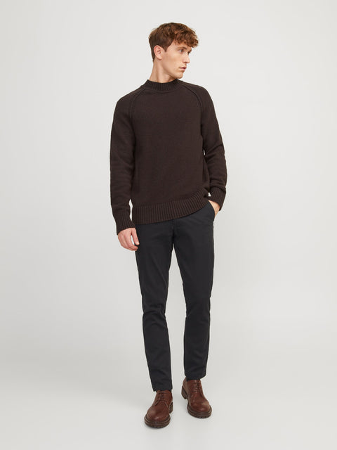 Man wearing a brown sweater and black pants on a white background