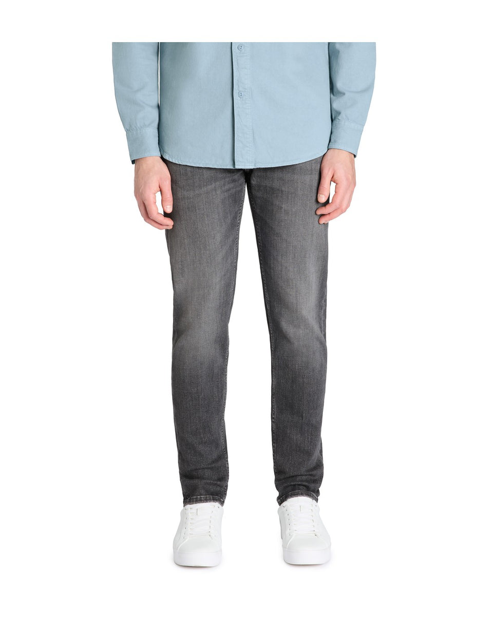 Person wearing a light blue shirt, gray jeans, and white sneakers on a white background