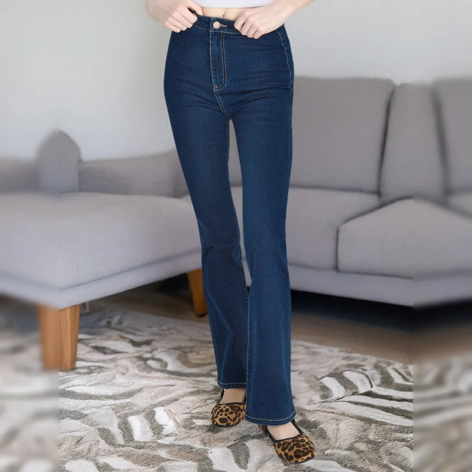 A person wearing dark blue high-waisted flare jeans, standing in a living room with a gray sofa and patterned rug.