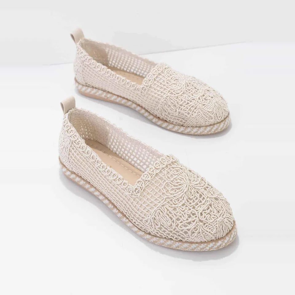 A pair of beige crochet slip-on shoes with braided jute soles, displayed on a clean white background.