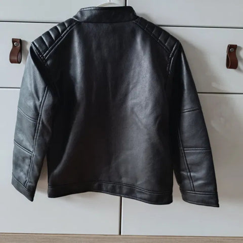 Black leather jacket on a white cabinet with wooden hooks.