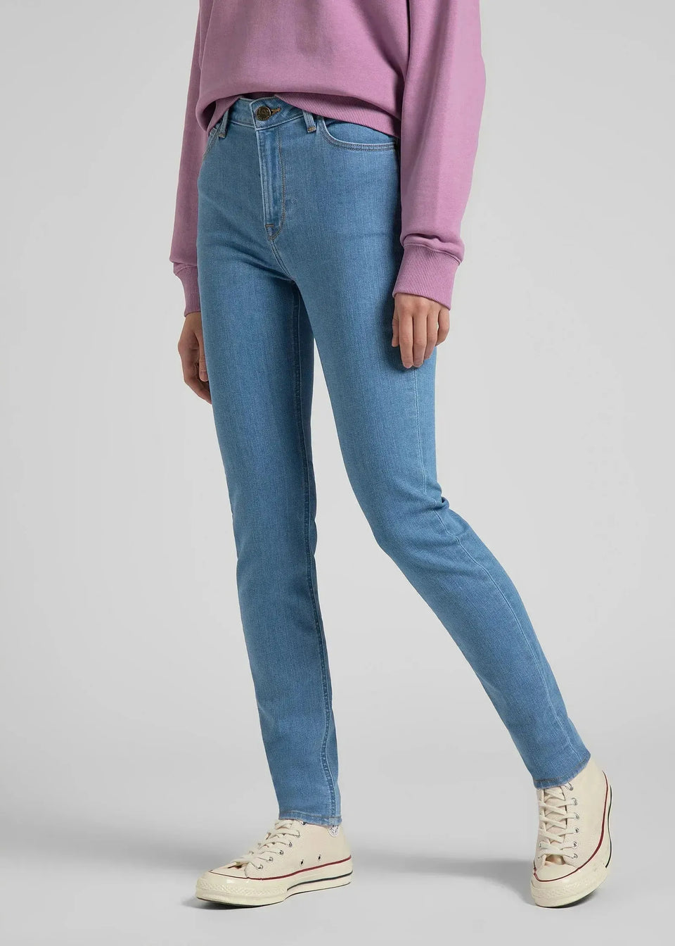 Person wearing blue jeans and a pink sweatshirt on a light gray background