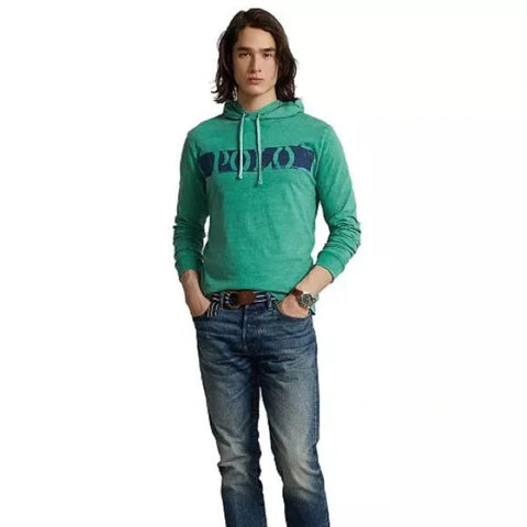 Person wearing a green hoodie with a logo and blue jeans on a white background