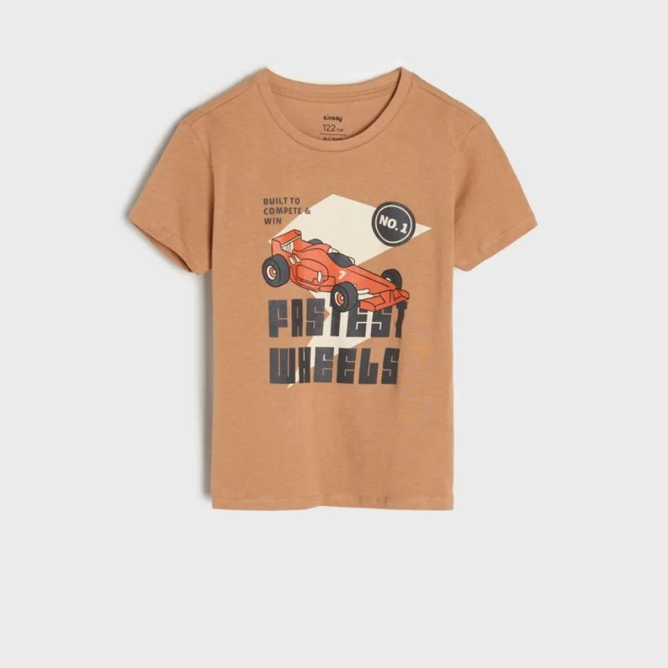 A kids' short-sleeve crewneck t-shirt in a warm tan/camel color, featuring a graphic of an orange race car and the text 'Fiestes Wheels' and 'No.1' on the front, displayed against a light gray background.