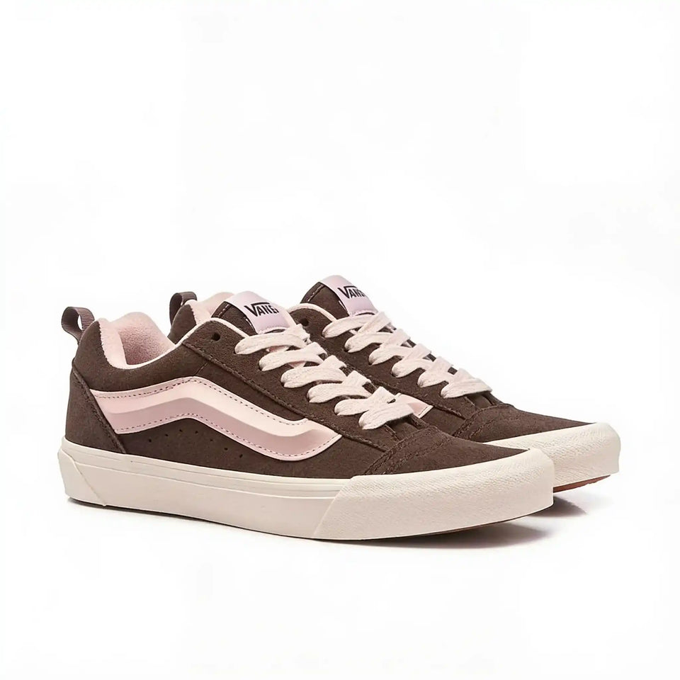A pair of Vans low-top sneakers in dark brown suede with light pink side stripes, matching pink laces, and cream-colored soles, shown against a plain white background.