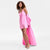 A model wearing a vibrant pink satin slip dress with a dramatic draped, oversized cape-like back drape and matching sheer sleeves, styled with clear high-heeled sandals against a plain white studio background.