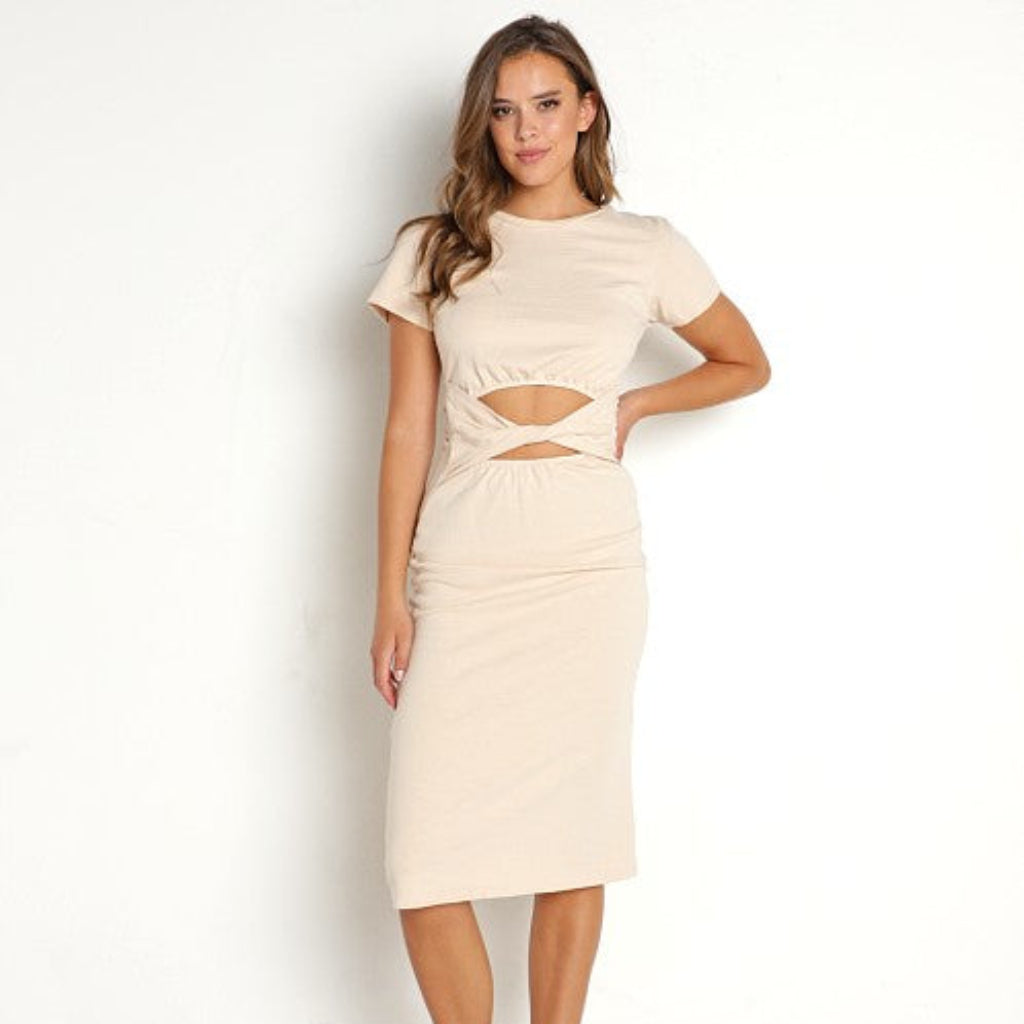 A woman modeling a beige short-sleeve midi dress with a twisted cutout detail at the waist, paired with black slide sandals, against a plain white studio background.