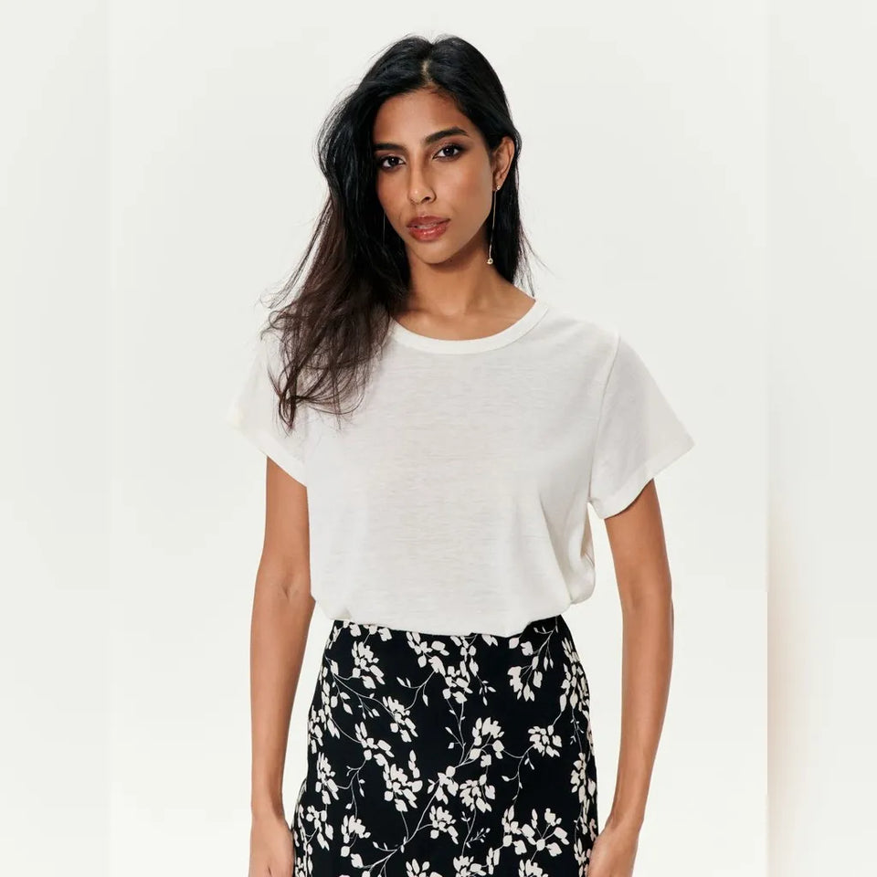 A woman modeling a white short-sleeve crewneck t-shirt paired with black and white floral print pants, set against a plain off-white background.
